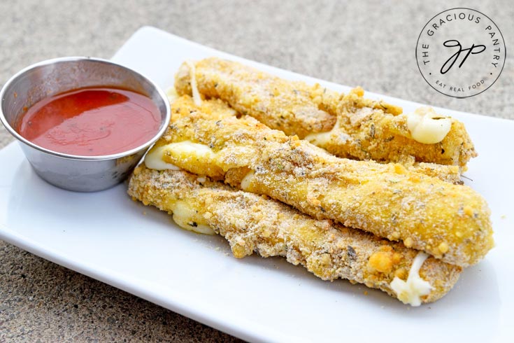 Clean Eating Air Fryer Cheese Sticks served on a white, rectangular plate with a small metal dish of marinara along side it.