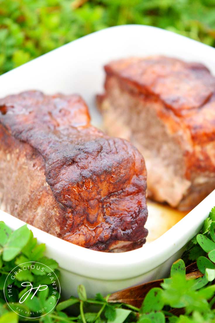 Clean Eating Asian Style Pork Chops shown up close in a white baking dish with a green, grassy background. They are freshly cooked and look deliciously golden brown.