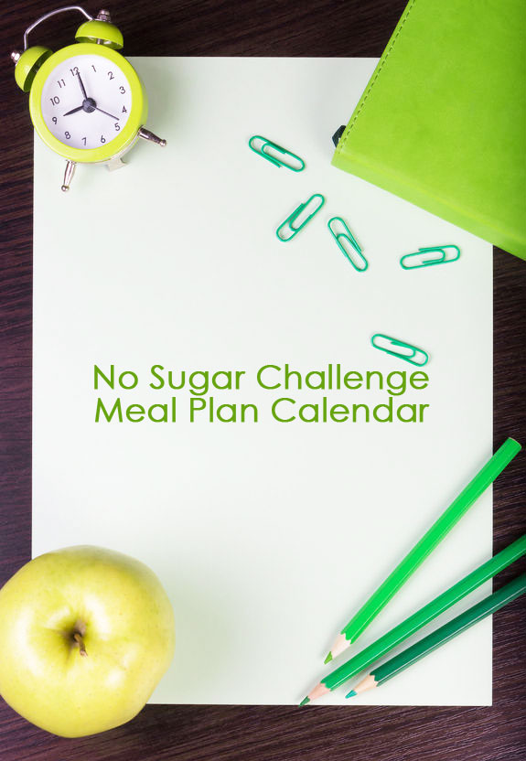 A piece of paper with the words, No Sugar Challenge Meal Plan Calendar written across it. There is a small clock, a green apple, and some green paper clips laying around the border of the paper.