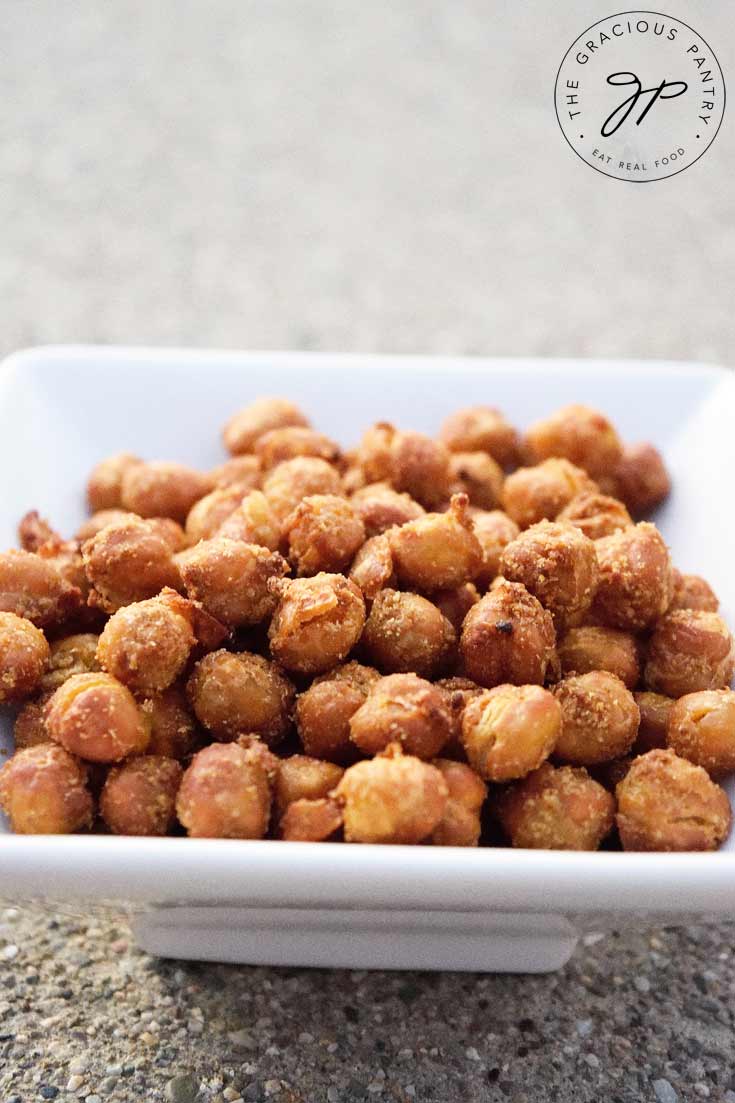 Clean Eating Air Fryer Roasted Chickpeas shown in a square, white bowl. The chickpeas are roasted to a golden brown color and look delicious and ready to eat!