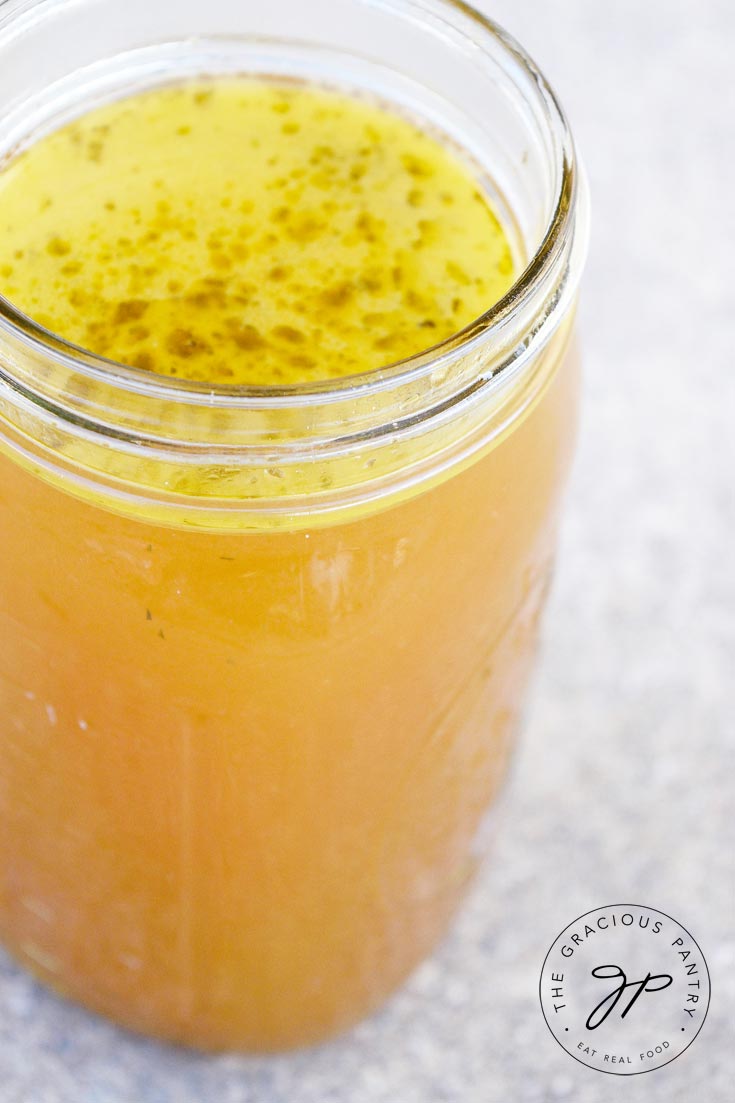Clean Eating Instant Pot Chicken Broth in a glass canning jar with the lid off. The broth has a few spices floating on top and is a deep gold in color.