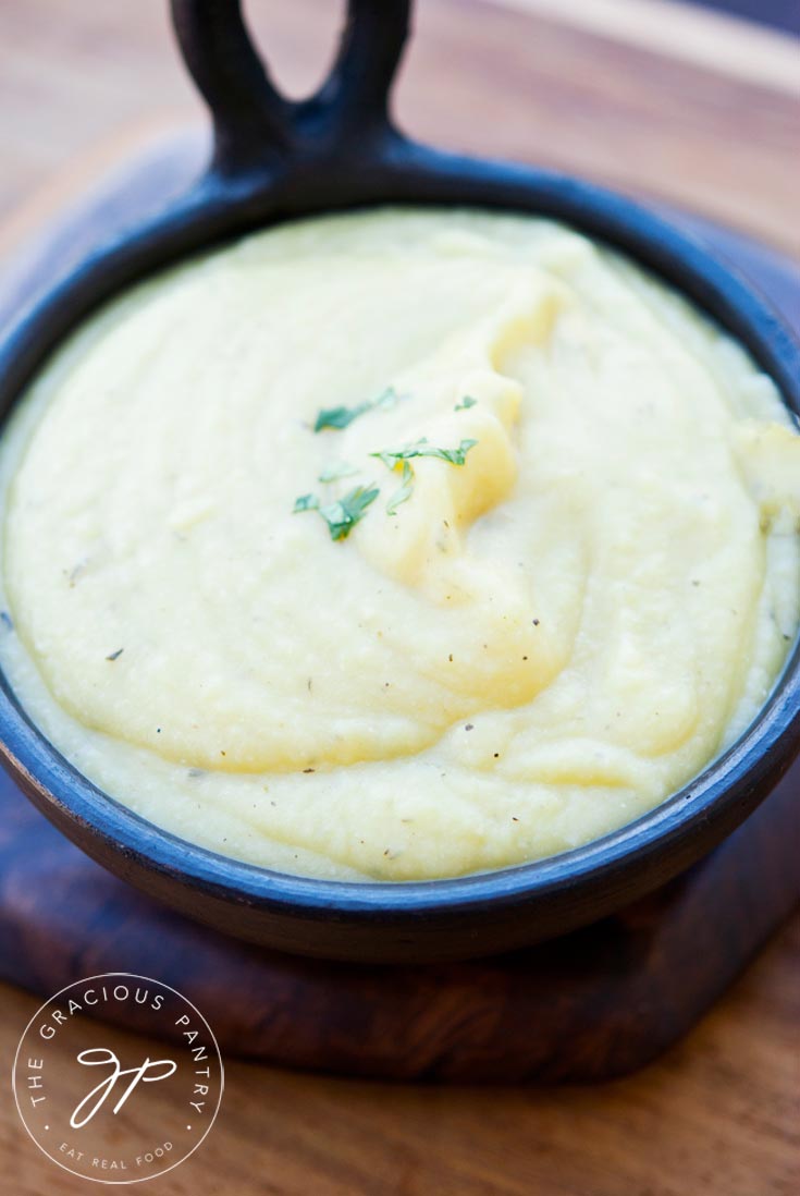 Clean Eating Potato Leek Soup in a black, ceramic bowl that has a handle. The off-white soup is topped with a tiny sprinkle of green, herb garnish.