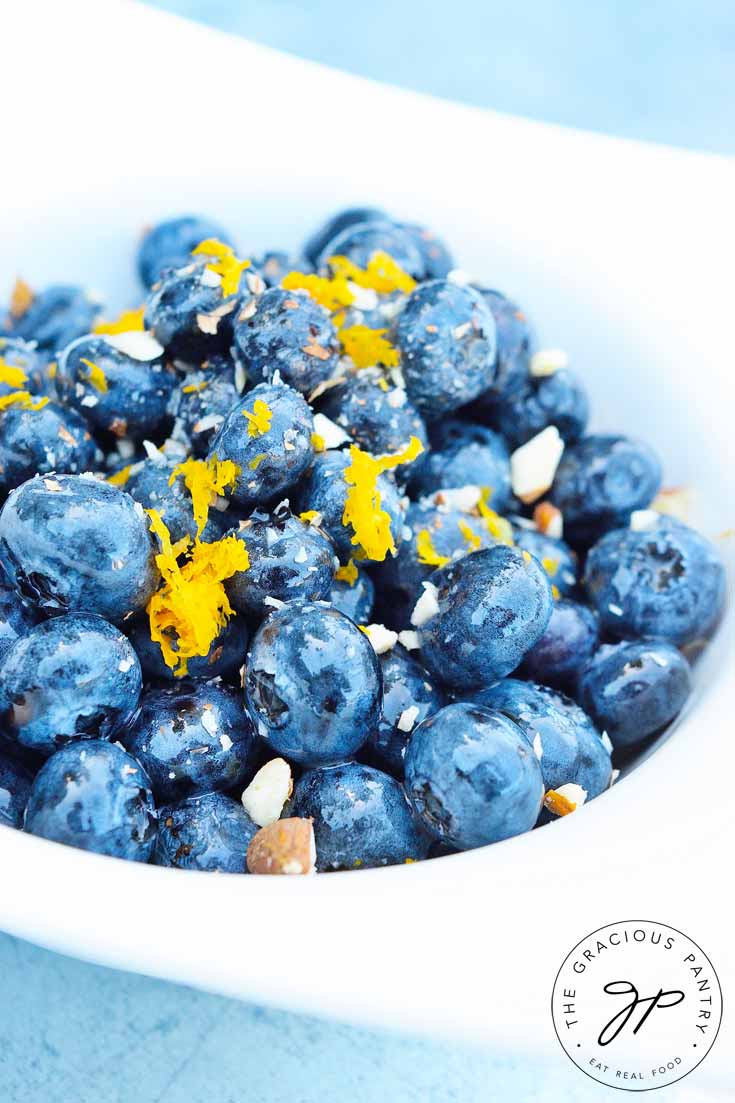 An up close shot of this Clean Eating Almond Blueberry Salad in a white bowl. The blueberries are a vibrant blue and have little bits of almonds and lemon zest sprinkled across the top.