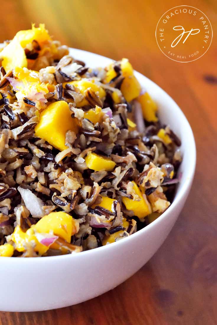 A close up shot of a white bowl filled with Clean Eating Mango Wild Rice Salad. The bowl sits off to the left side of the photo so you can see about half of the bowl.