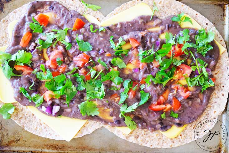 And overhead shot of this Clean Eating Loaded Sheet Pan Quesadillas shows the recipe just before the top layer of tortilla has been added. You can see the refried beans, tomatoes, onions and cilantro spread beautifully around the surface of the bottom layer of tortillas.