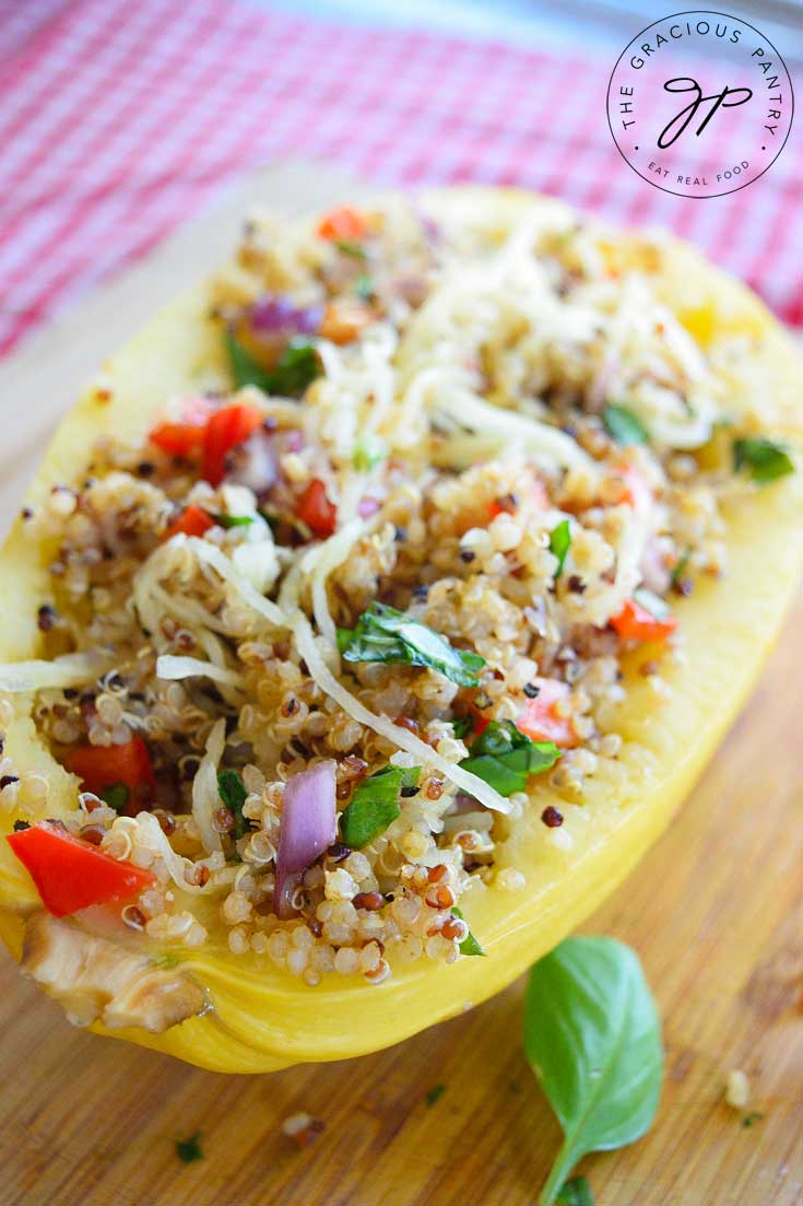 This Clean Eating Quinoa Stuffed Spaghetti Squash Recipe photo shows a half of a spaghetti squash stuffed with a pretty, quinoa salad. You can see bits of the red pepper and purple onion mixed in with the quinoa.