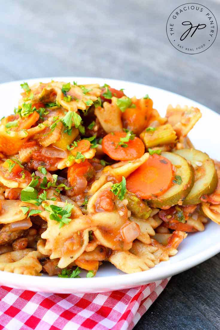 An up close shot of this Clean Eating Summer Vegetable Bow Tie Pasta shows the pasta on a white plate with chunks of zucchini and carrots visible between the noodles and sauce.