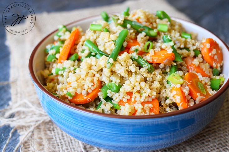 A broader view of this Clean Eating Green Bean Quinoa Salad shows the entire bowl sitting on a piece of burlap. The green beans and carrots are a vibrant green and orange mixed into a sea of light brown quinoa. You can also see bits of green onion mixed in as well.