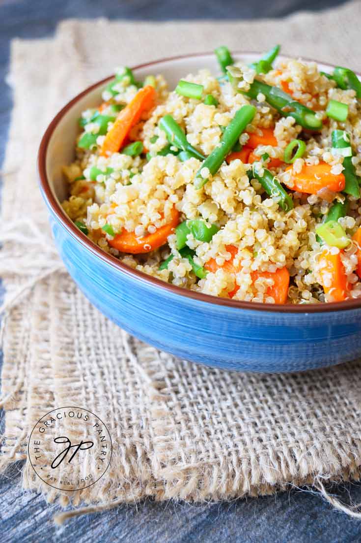 An up close shot of this Clean Eating Green Bean Quinoa Salad shows the salad on a blue bowl. The carrots and green onions are vibrant and clearly visible mixed in with the quinoa.