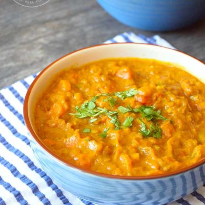 A blue bowl filled with Instant Pot Lentil Curry and garnished with fresh greens.