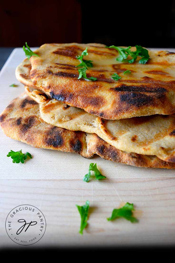 four garlic seasoned grilled flatbread garnished with fresh parsley stacked on a cutting board