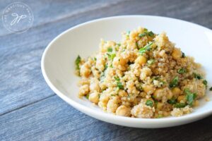 A white bowl sits on a gray surface, filled with Chickpea Quinoa Salad.