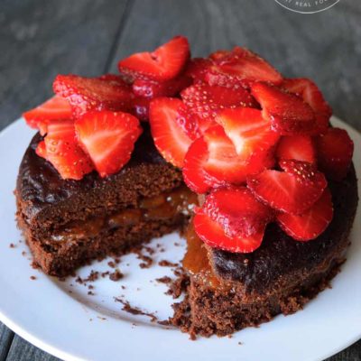 A front view of this Instant Pot chocolate cake on a white platter, topped with strawberries.