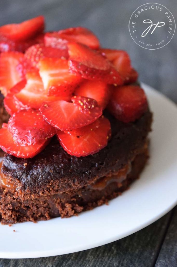 An up close shot of an Instant Pot chocolate cake sitting on a white platter, topped with fresh strawberry slices.
