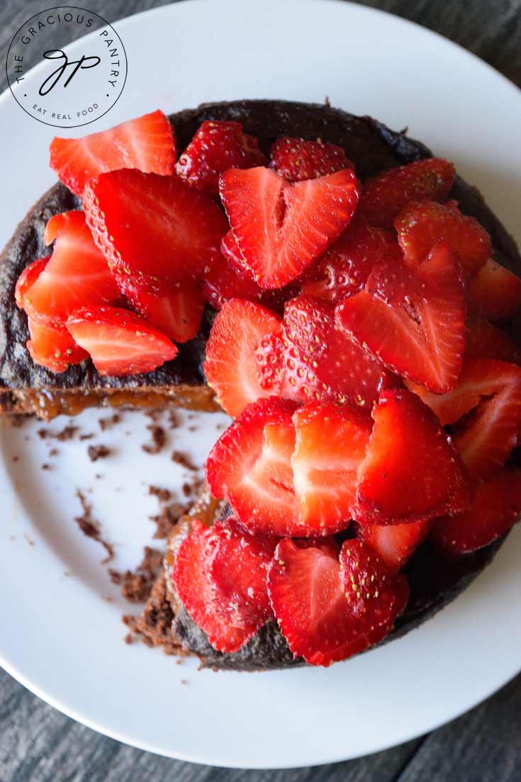 An overhead view shows one slice removed from the cake and some of the fruit spread filling in the center. The cake is topped with sliced strawberries.