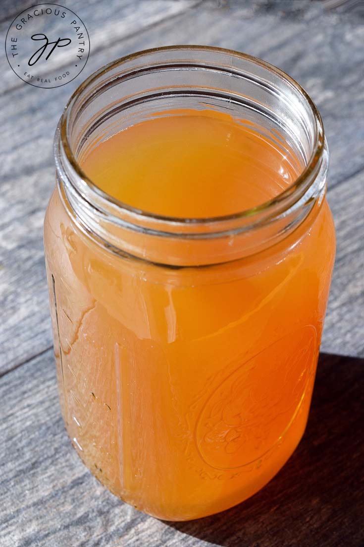 A single jar of this Clean Eating Vegetable Stock sits on a table with it's lid off. You can see into the jar. The broth is a dark, golden brown color.