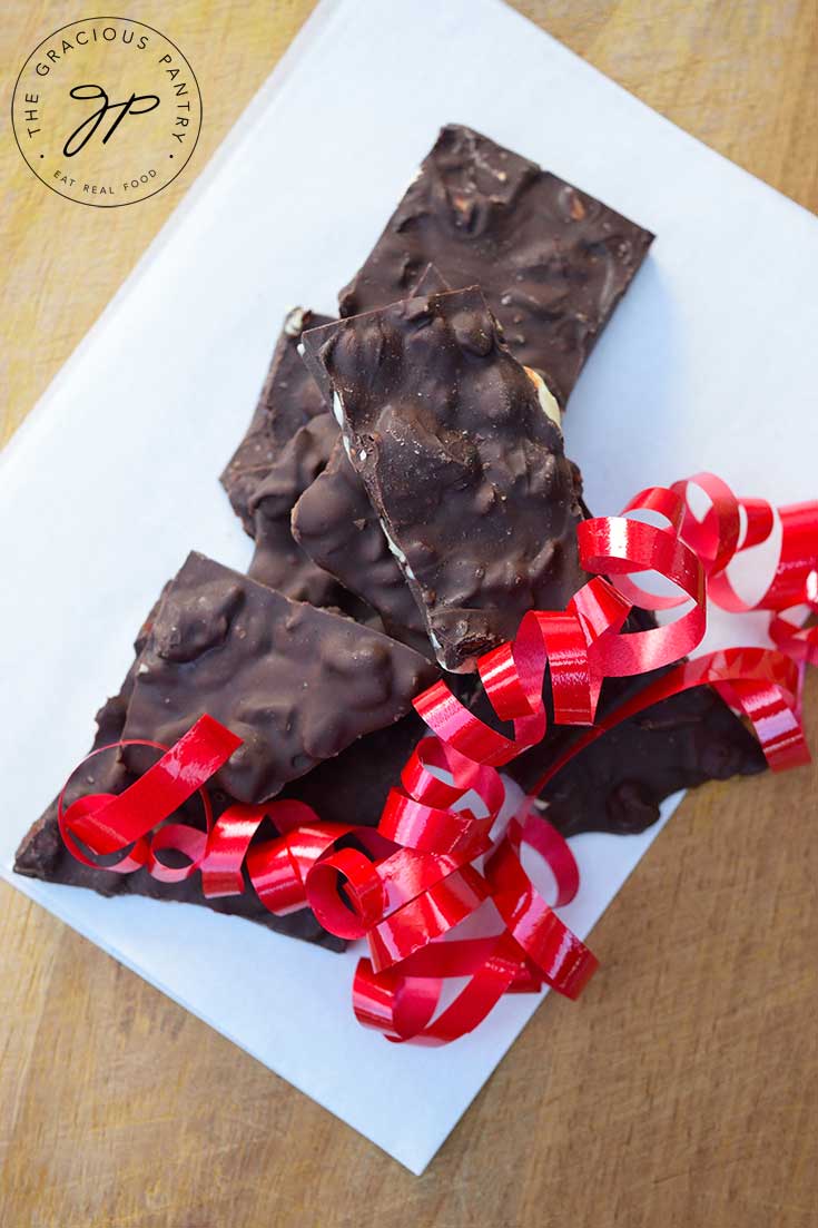 An overhead view of several pieces of Chocolate Bark sitting on white parchment paper with a red ribbon laying to the side of the pile.