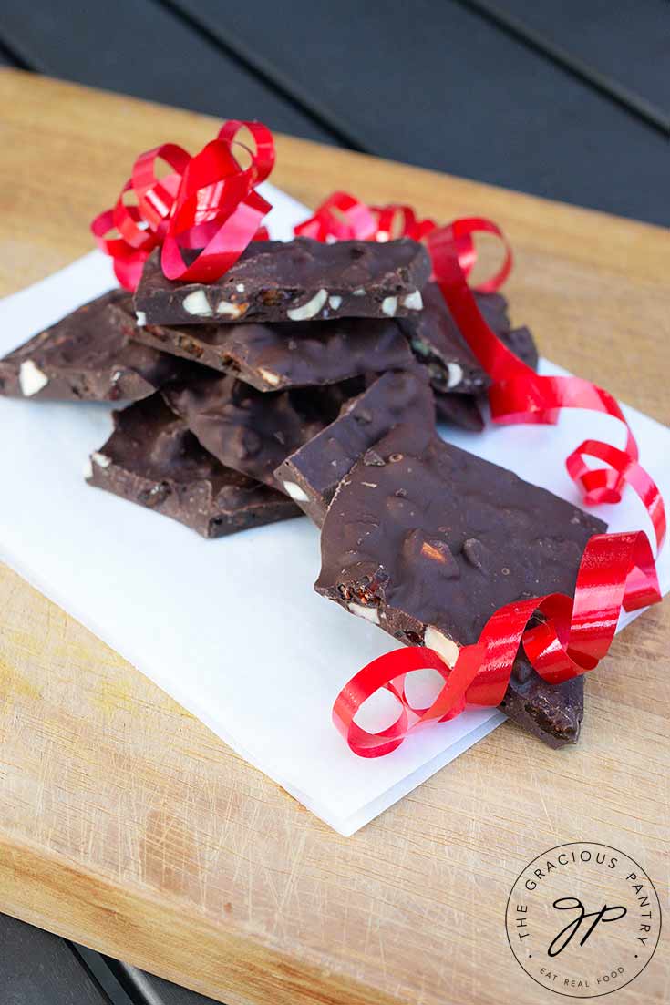 A side view of a pile of Chocolate Bark sitting on some white parchment paper. The chocolate bark has a single red ribbon laying over the side of it.