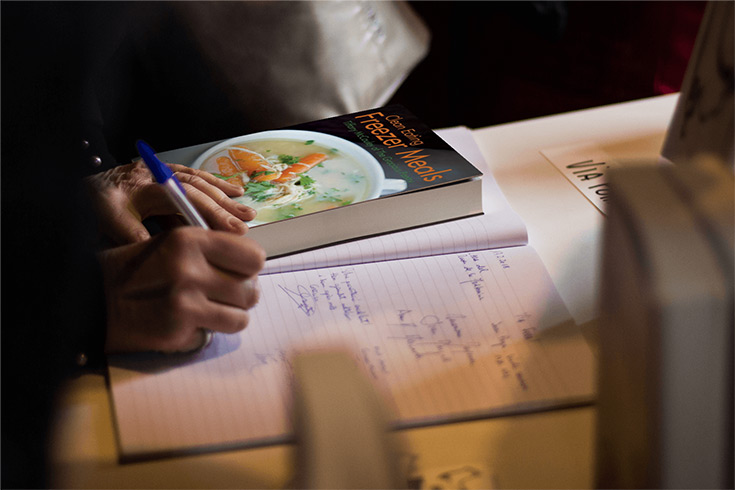 Woman making her shopping list with the clean eating freezer meals cookbook sitting next to her.