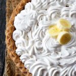 A whole, clean eating banana cream pie shown from overhead. You can see the layer of swirled whipped cream on top with three slices of banana in the middle.