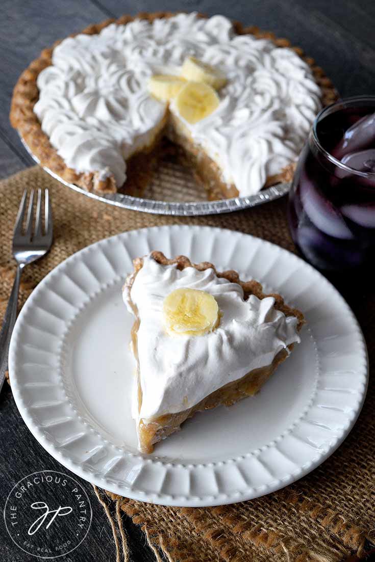 The cut, clean eating banana cream pie is sitting in the background while a white plate with a single slice of pie sits to the front.