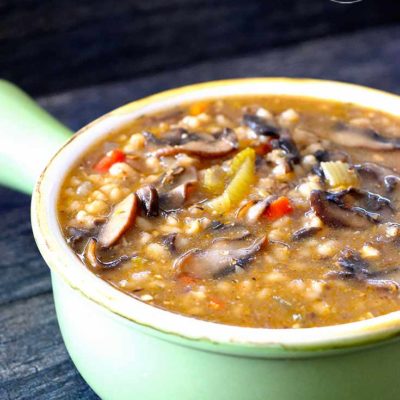 An up close shot of this mushroom barley soup shows the soup in a green bowl with a handle. You can see bits of the carrots and celery along with quite a few mushroom slices.