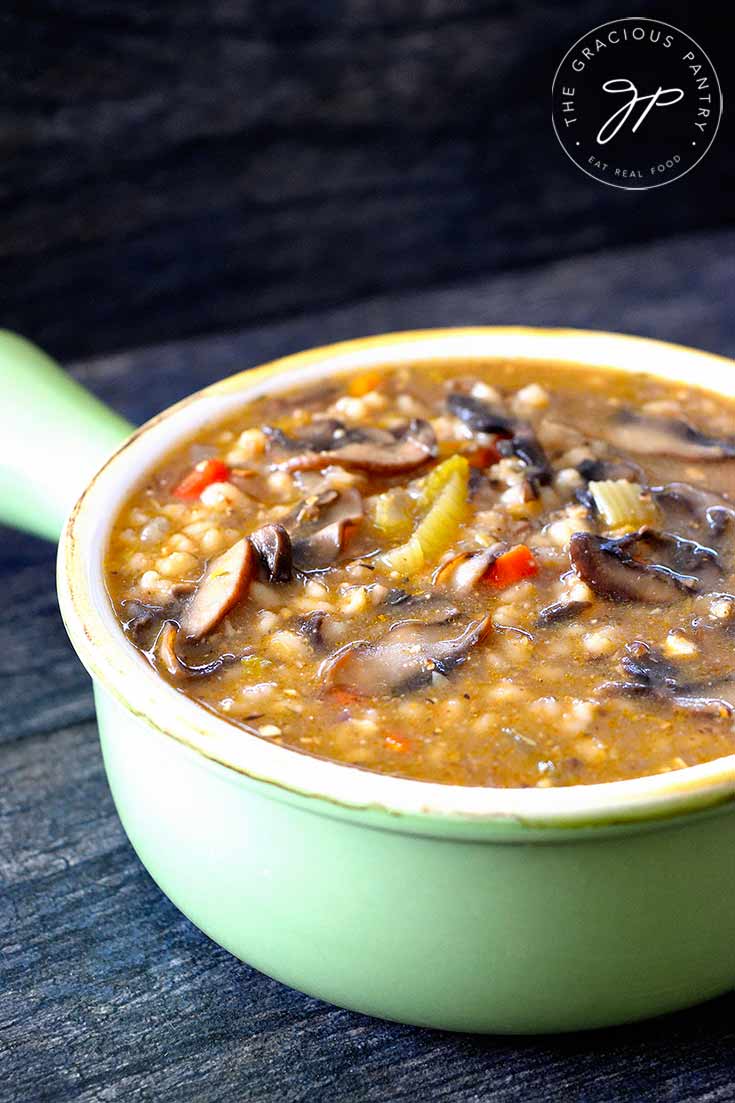 An up close shot of this mushroom barley soup shows the soup in a green bowl with a handle. You can see bits of the carrots and celery along with quite a few mushroom slices.