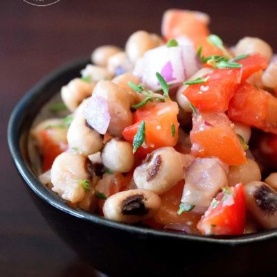 This clean eating black eyed pea salad recipe is displayed in a small, round, black bowl. You can see the beans, tomatoes, peppers and fresh herbs.