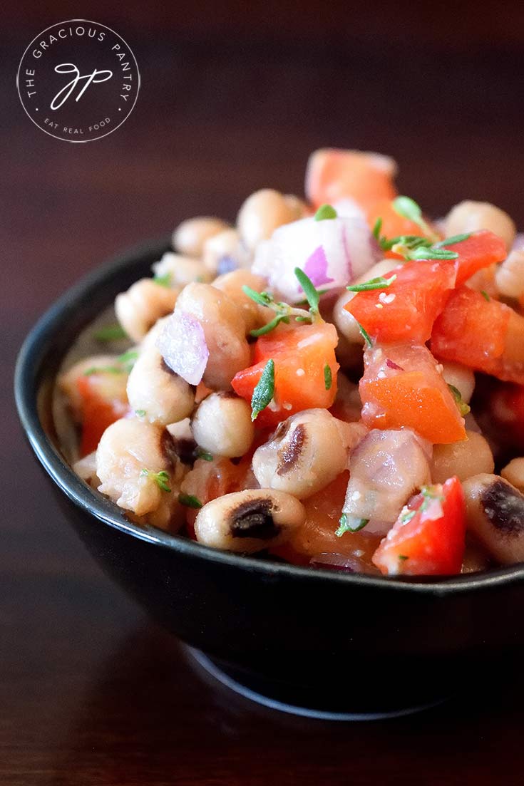 This clean eating black eyed pea salad recipe is displayed in a small, round, black bowl. You can see the beans, tomatoes, peppers and fresh herbs.