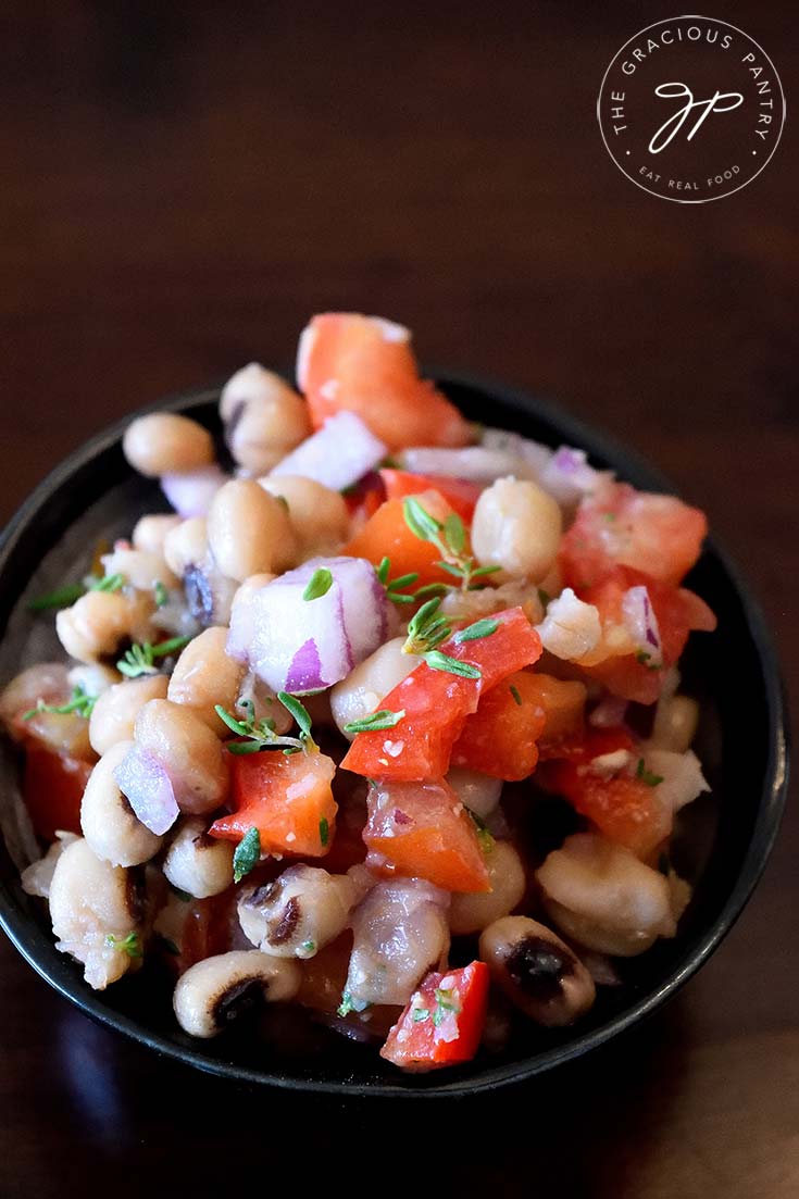 An overhead shot looking downwards at a bowl filled with thsi clean eating black eyed pea salad filled with fresh tomatoes, peppers and chopped, fresh thyme. Delicious!