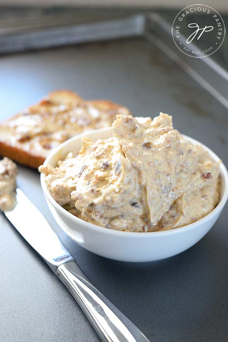 A small white bowl sits filled with this clean eating date butter. A knife sits to the left of the bowl and a piece of toast sits behind the bowl with the spread already on it.