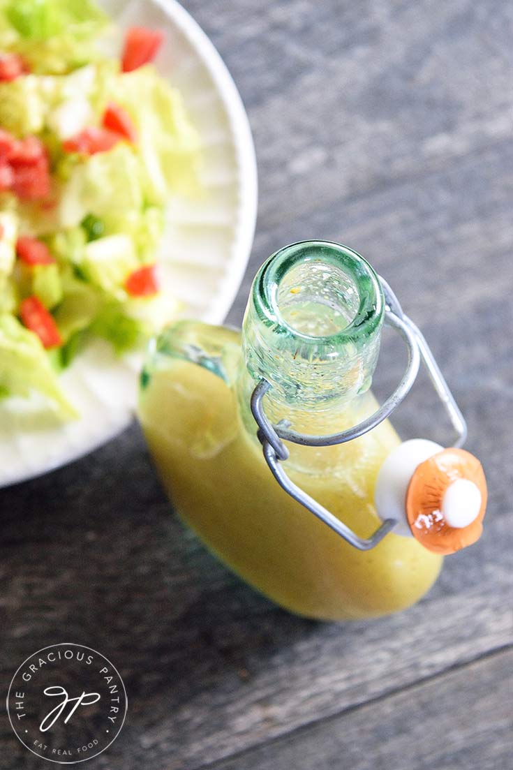 An overhead view of a bottle of this Mustard Vinaigrette sitting next to a green salad with red tomatoes, ready to eat.