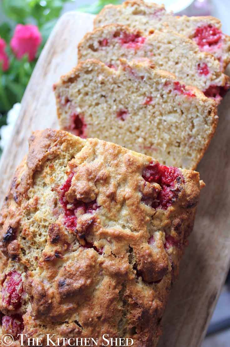 A few slices are cut and laying next to this loaf of Clean Eating Raspberry Vanilla Banana Bread.