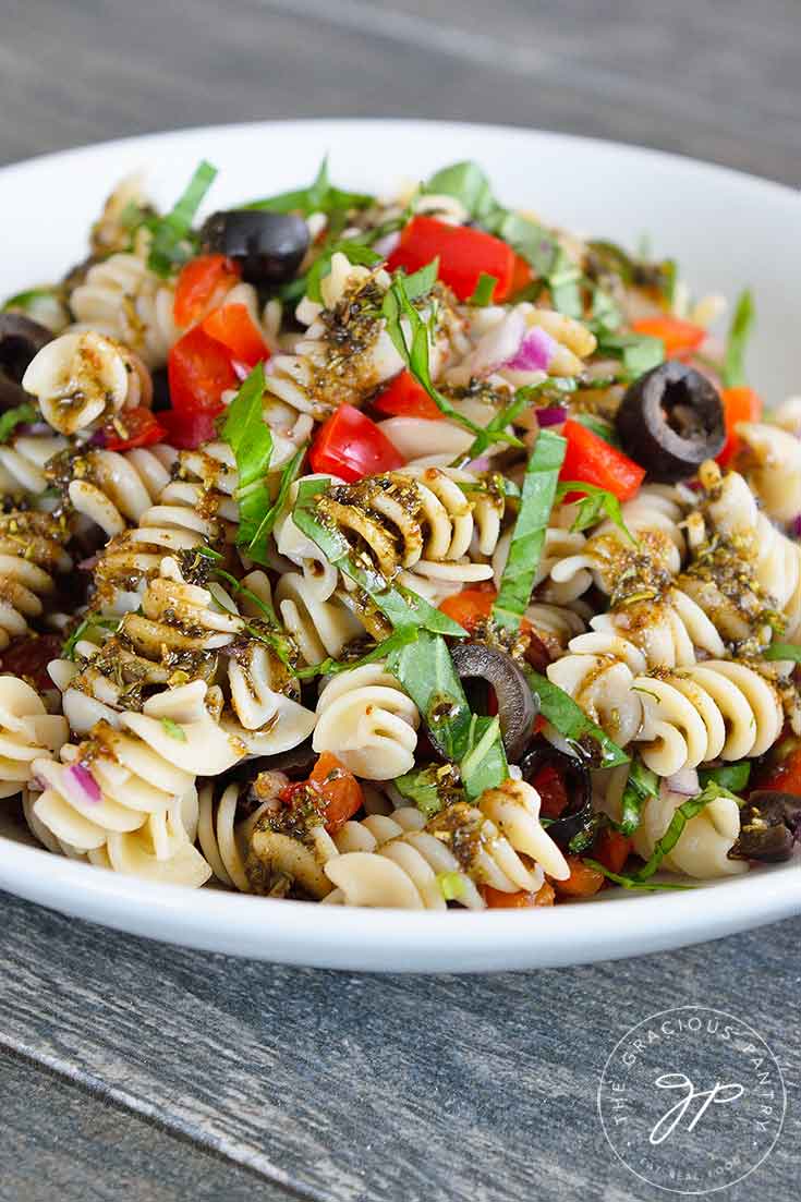 A side view of this healthy, Rustic Italian Pasta Salad Recipe shows the pasta, red peppers and fresh basil in a white bowl.