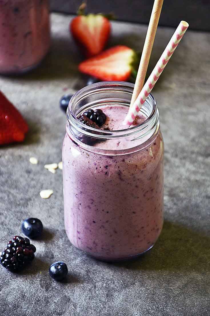 A head on view of a mason jar filled with this Mixed Berry Smoothie. It has two straws in it and a couple of blackberries. Several cut strawberries sit in the background.