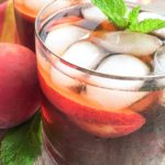 A side view of this clean eating peach iced tea recipe shows the tea in a clear glass with ice cubes and a sprig of fresh mint at the top of the glass.