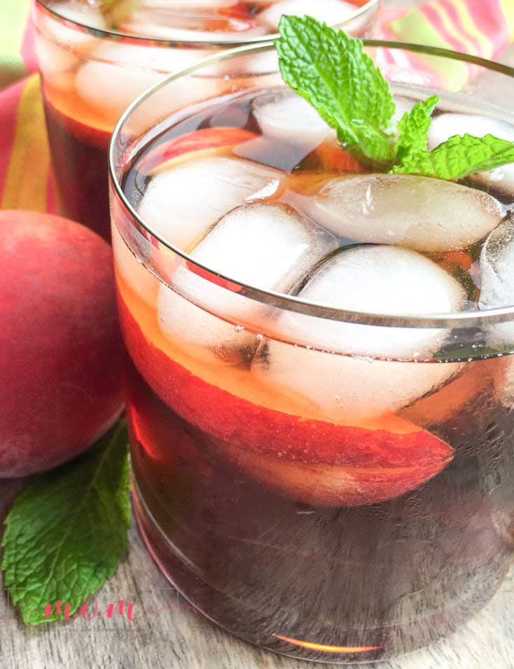 A side view of this clean eating peach iced tea recipe shows the tea in a clear glass with ice cubes and a sprig of fresh mint at the top of the glass.