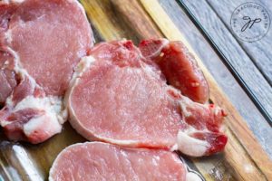 A set of pork chops ready to prep for the air fryer, sitting on a cutting board.