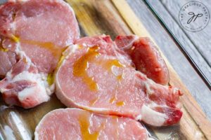 Pork chops on a cutting board, drizzled with a small amount of oil.