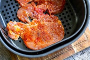 Seasoned pork chops in the air fryer basket, ready to cook.