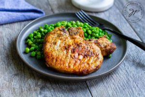 Air fried pork chops on a plate with a side of green peas.