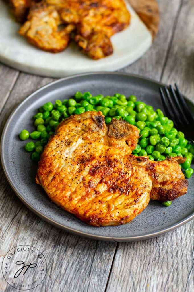 A plate of air fried pork chops sits next to a side of peas with left over pork chops sitting on a board to the side.