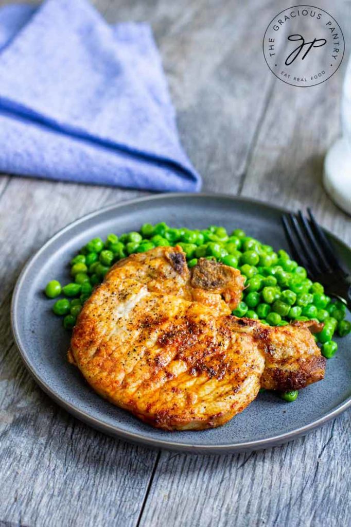 A plate of air fryer pork chops with a side of peas sits on the table next to a blue napkin,