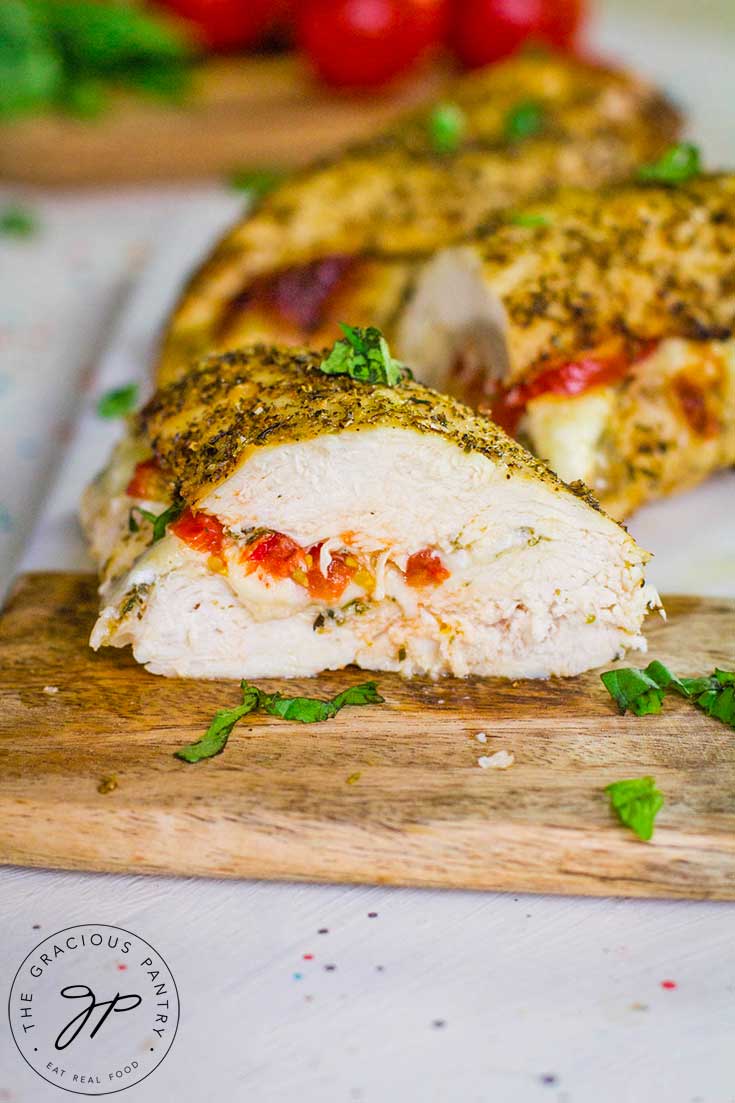 A half of a chicken breast sits, cut side visible, on a cutting board. You can see the tomato and cheese in the middle of the breast.