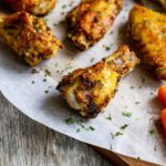 A cutting board with air fryer chicken wings sits with a small pile of baby carrots next to it.