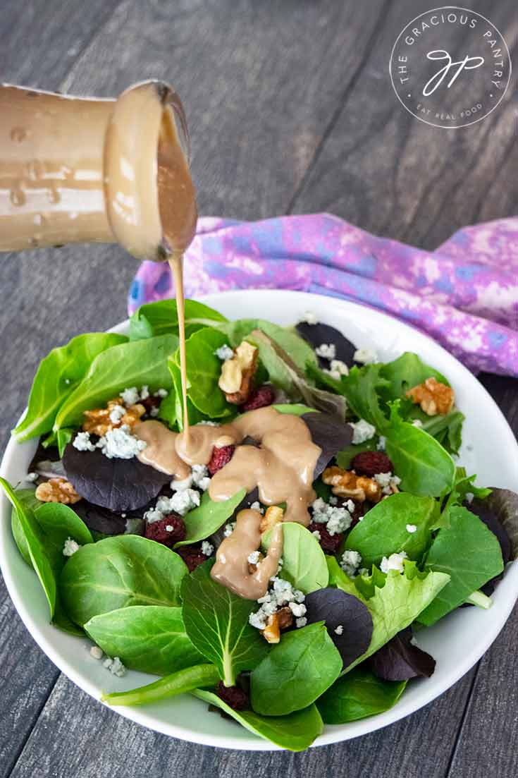 A beautiful bowl of cranberry walnut salad sits on a table and this blue cheese vinaigrette is being poured over the top.