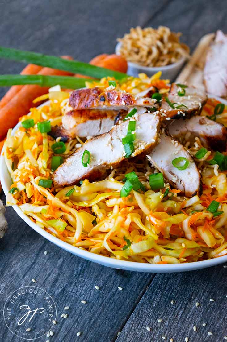 A delicious Chinese Chicken Salad sits on a table, ready to eat. It has carrots and green onions laying behind the bowl.