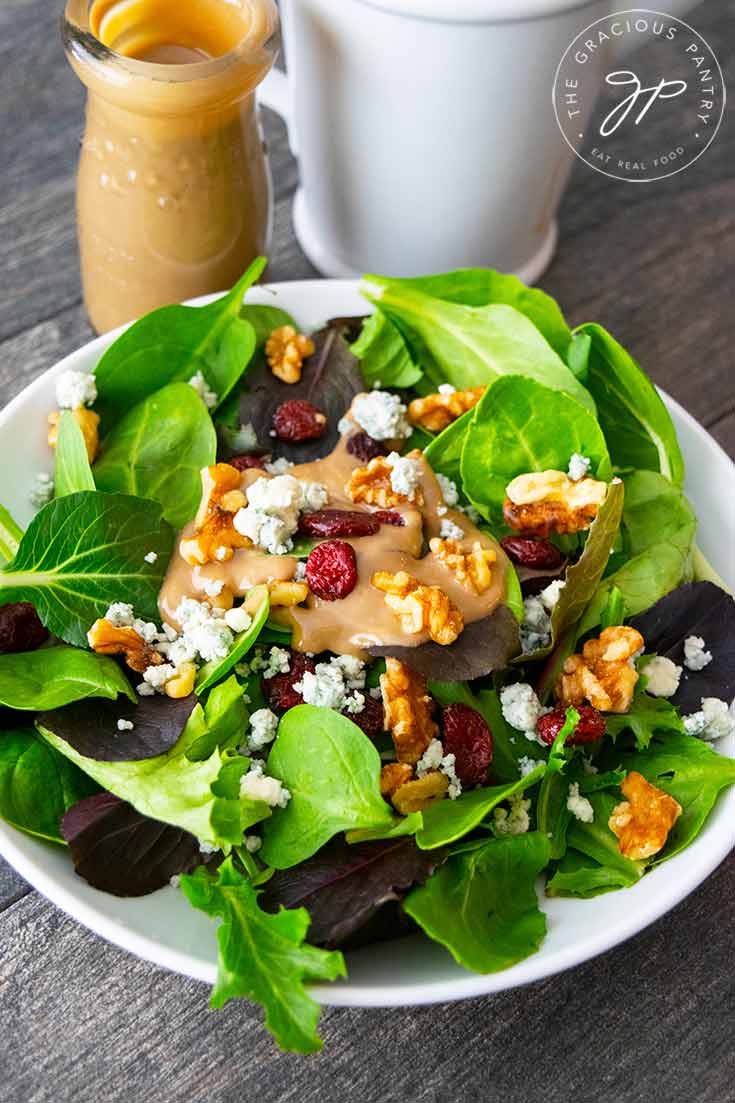 A bowl of this Cranberry Walnut Salad sits next to a jar and mixing pitcher of the blue cheese vinaigrette I used on this salad.