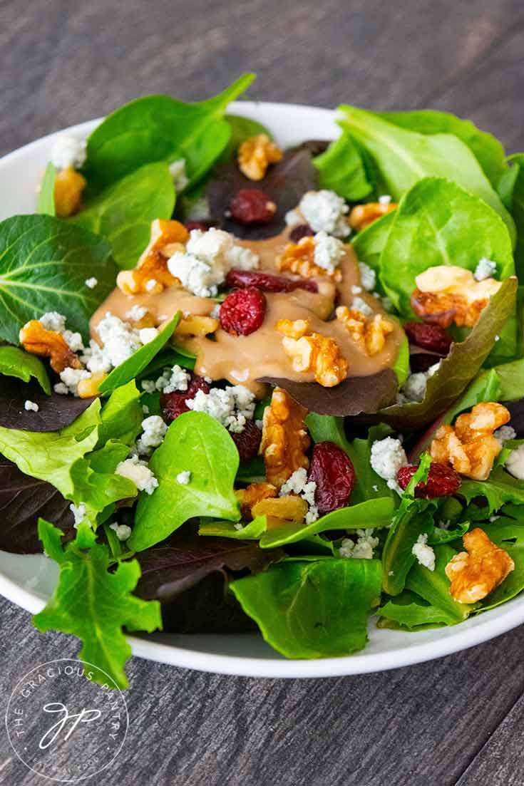 A side view of this Cranberry Walnut Salad shows the varied lettuces in the spring mix, the bright red cranberries and golden brown walnuts with sprinkles of blue cheese crumbles.