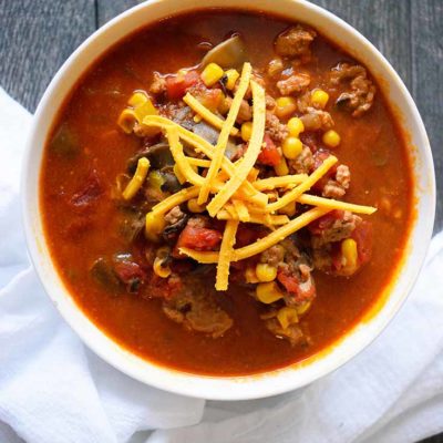 And overhead view of this Instant Pot Turkey Chili in a white bowl. You can see bits of turkey and corn and tomatoes with shredded cheddar sprinkled over the top.